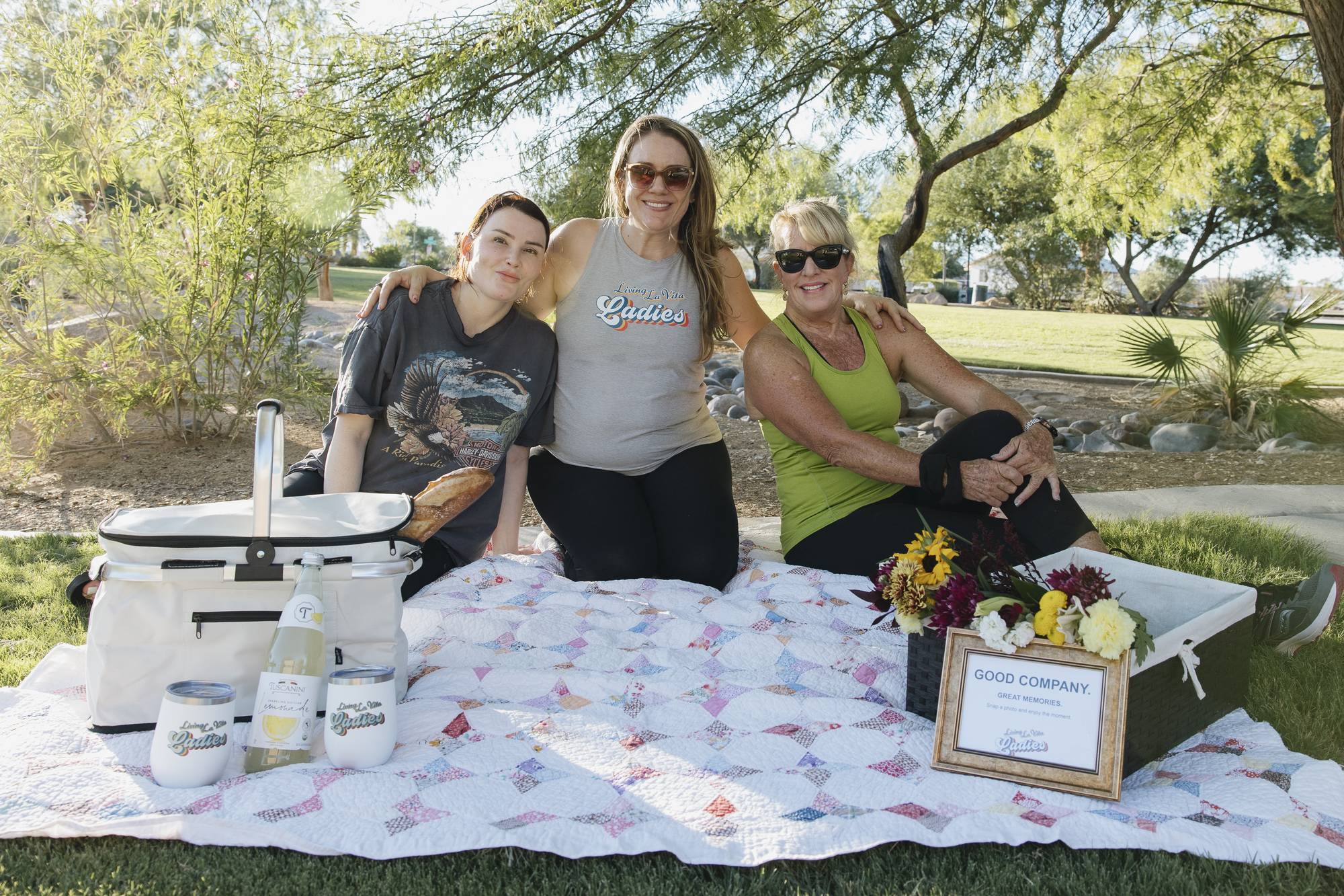 Three women smile on a picnic blanket at the La Vita Ladies goat yoga welcome setup