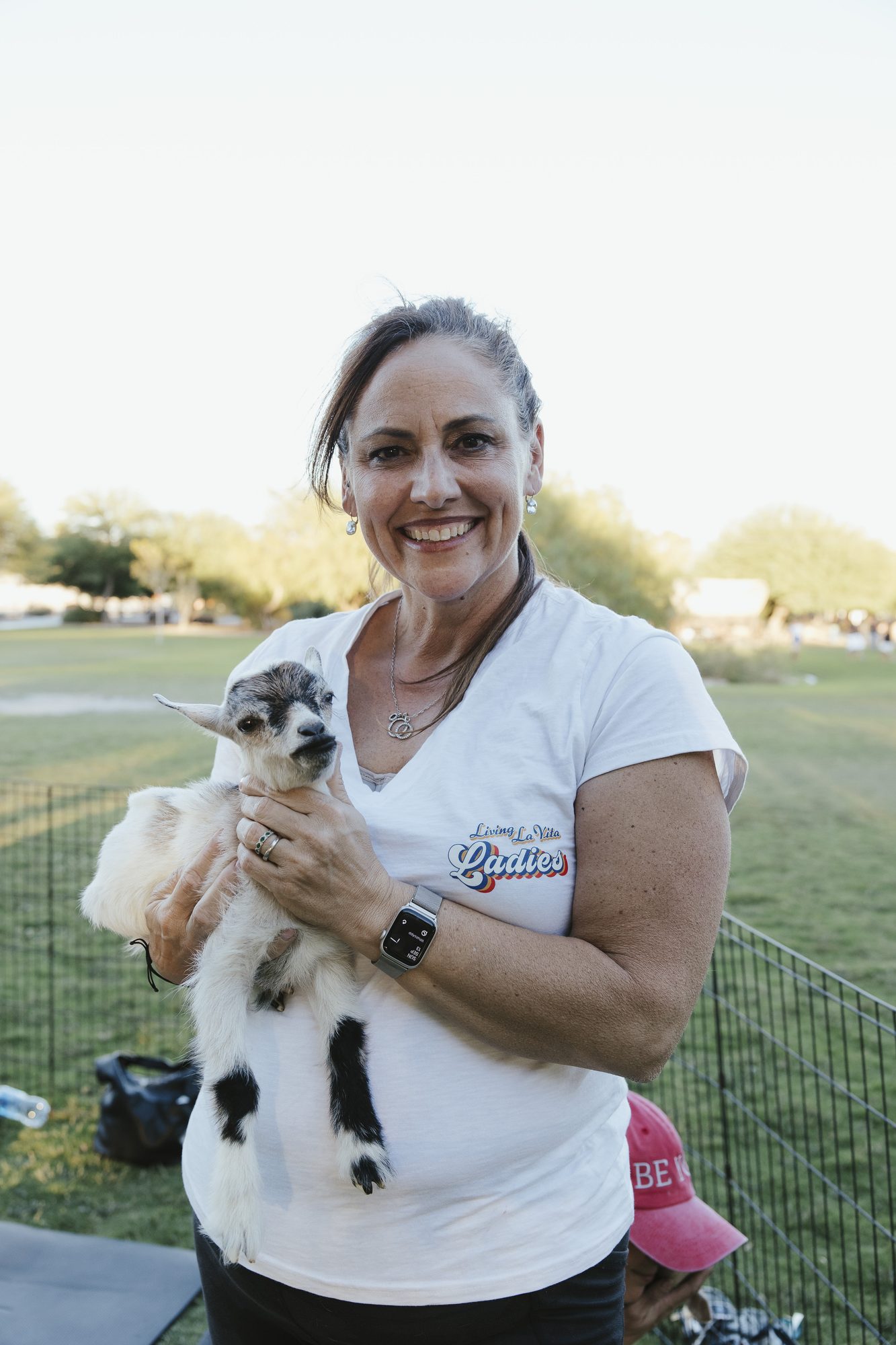 A woman in a white shirt holds a baby goat and smiles