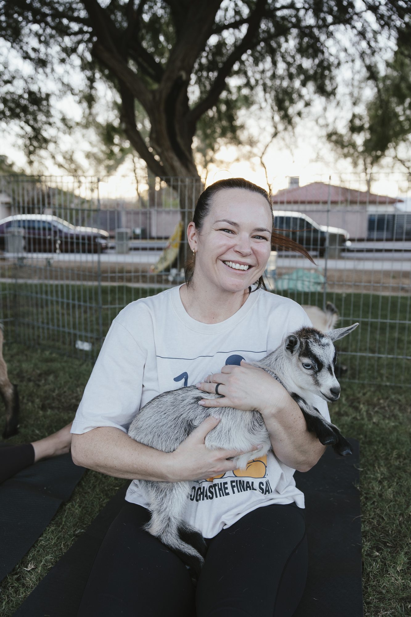 A woman sits on her yoga mat cradling a gray goat