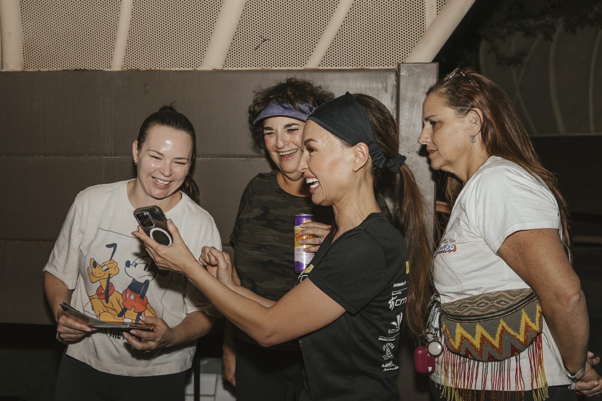 Four women laugh together over a phone at the after-yoga gathering